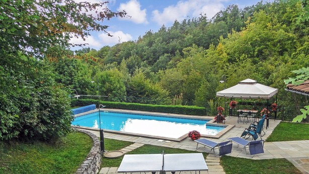 Ein Schwimmbad mit umlaufender Sonnenterrasse, einem Pavillon und Sitzmöglichkeiten im Freien.