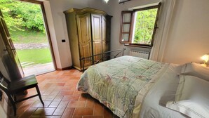 Ein Schlafzimmer mit Bett, Stuhl, Kleiderschrank, Fenster und einer Tür zu einem Garten.