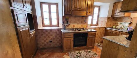 Uma cozinha com armários de madeira, painel de azulejos, fogão a gás e uma janela.