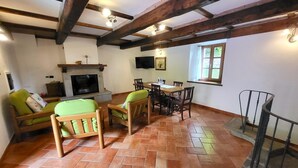 Ein möbliertes Wohnzimmer mit Kamin, Holzbalken, Essbereich und einer Treppe.