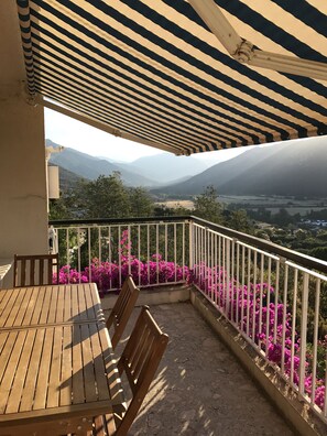 A balcony with a wooden table and chairs, a white railing, and pink flowers. - Family villa in Corsica with fabulous sea views (Vico)