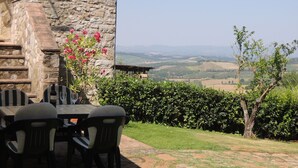 An outdoor patio with stone walls, a table with chairs, and a view of rolling hills. - Tuscany. Lovely holiday home with swimming pool. (Castellina in Chianti)