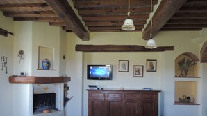 A dining area with a tiled floor, wooden ceiling beams, a fireplace, a television, and a table with a colorful tablecloth. - Tuscany. Lovely holiday home with swimming pool. (Castellina in Chianti)