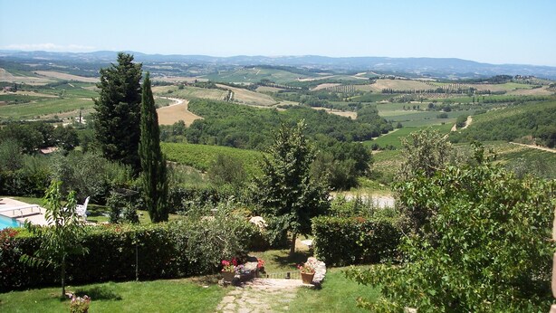 A lush landscape with rolling hills, a clear sky, and a pathway leading through a garden with potted plants and a small building. - Tuscany. Lovely holiday home with swimming pool. (Castellina in Chianti)