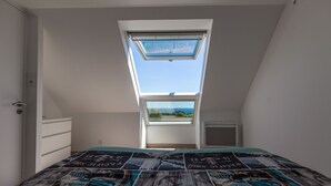 A bedroom with a skylight, a bed with a patterned bedspread, and a view of a landscape through the skylight.