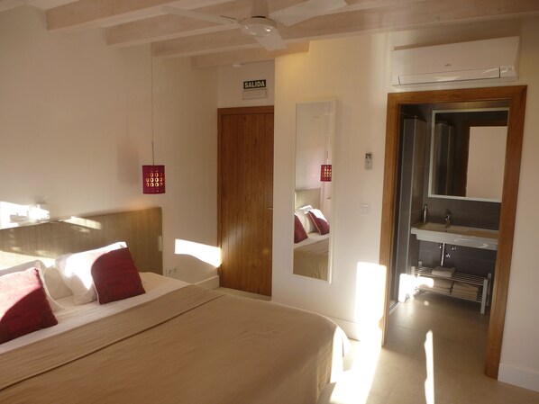 Habitación de hotel con cama, cabecera de madera, baño con lavamanos y espejo, y una puerta que indica 'SALIDA'.