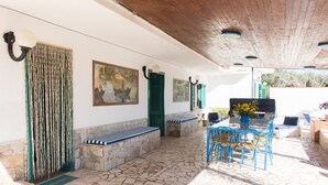 Patio in pietra con posti a sedere all'aperto, un barbecue e opere d'arte alle pareti.
