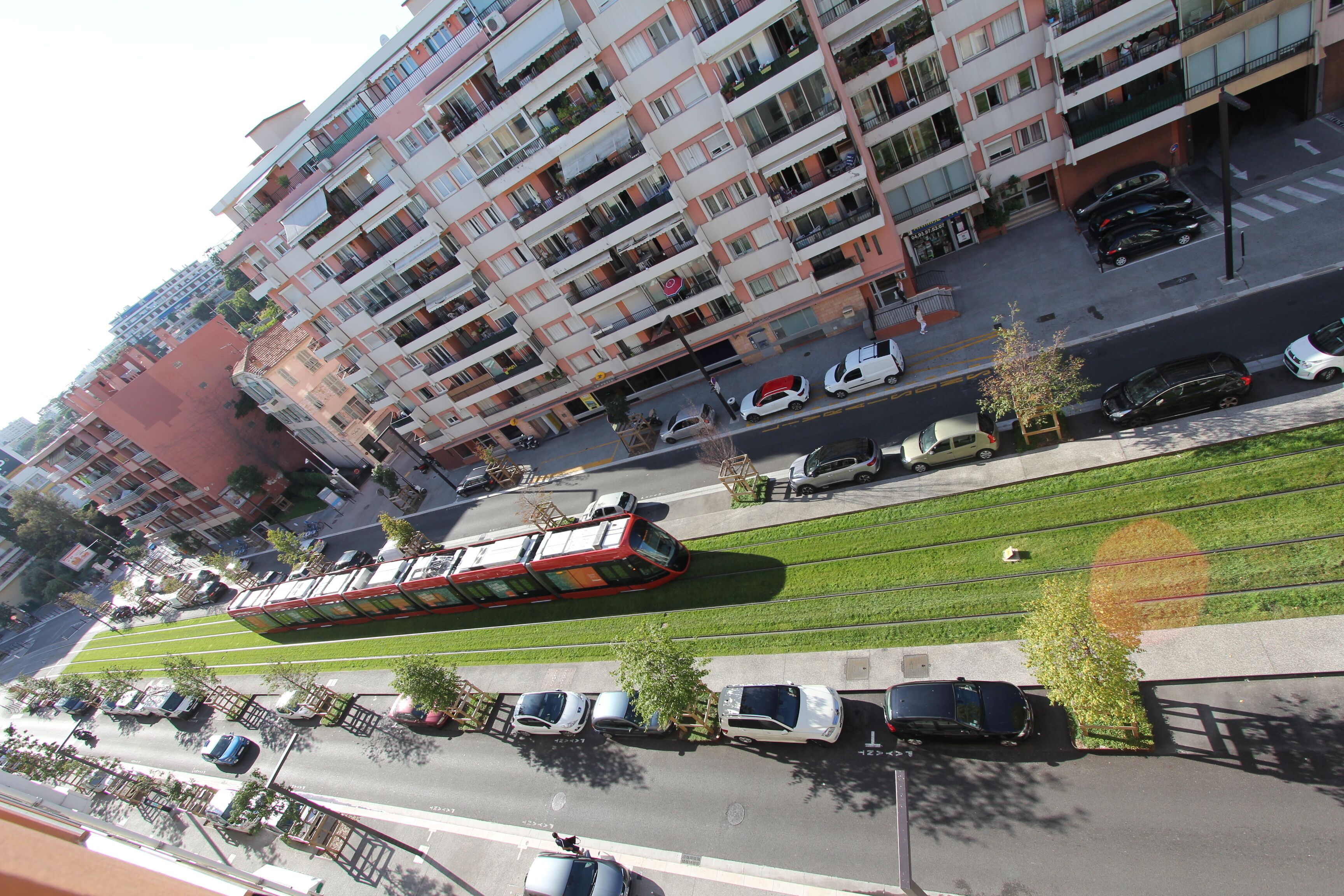 A multi-story residential building with balconies, a tram line, and parked cars.