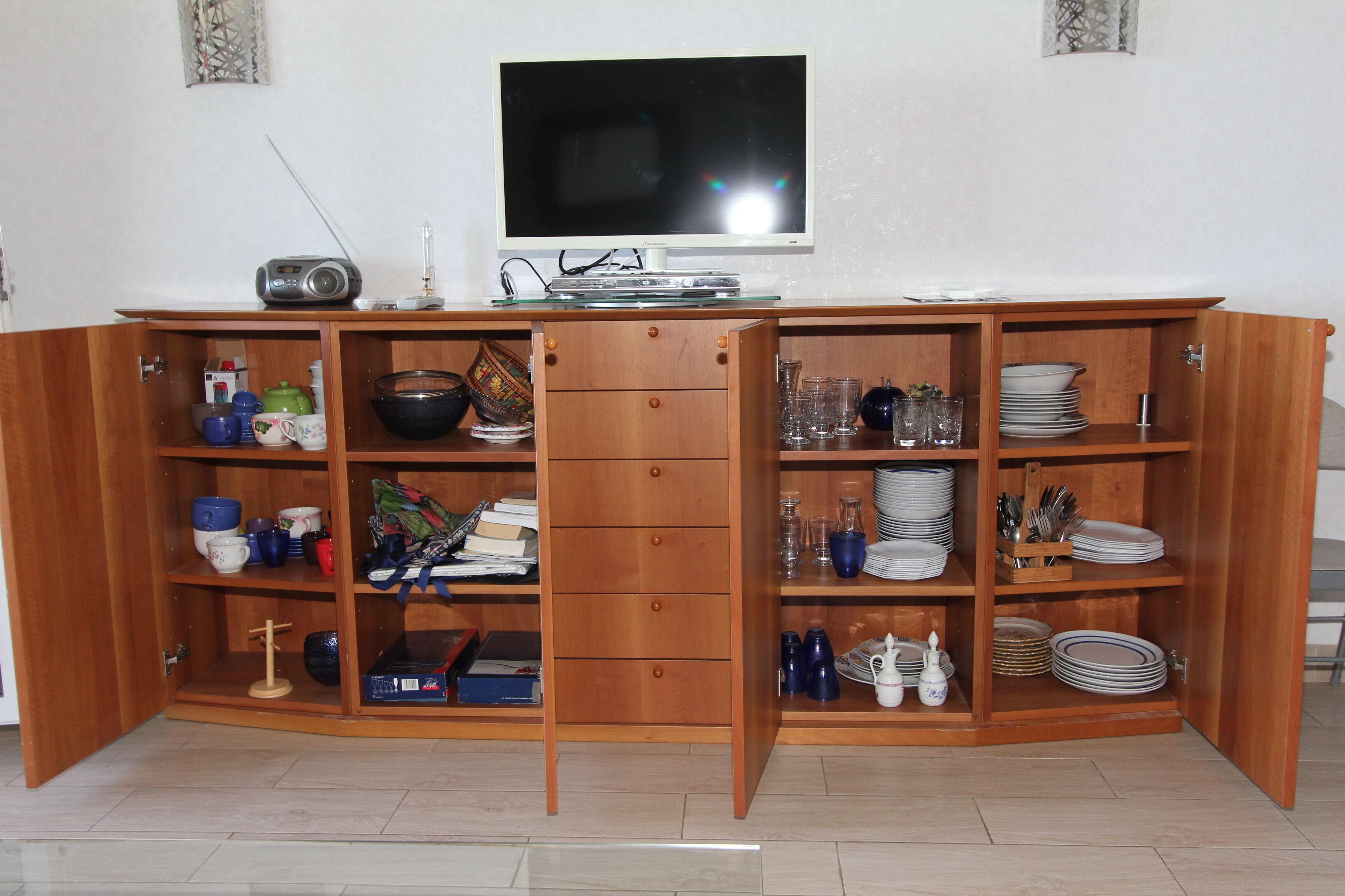 A wooden cabinet with shelves containing kitchenware, a television, and a radio.
