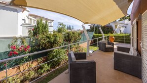 Un patio al aire libre con mobiliario de mimbre, una vela de sombreo grande y vistas del vecindario circundante.