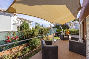 An outdoor patio area with wicker furniture, a large shade sail, and a view of the surrounding neighborhood.
