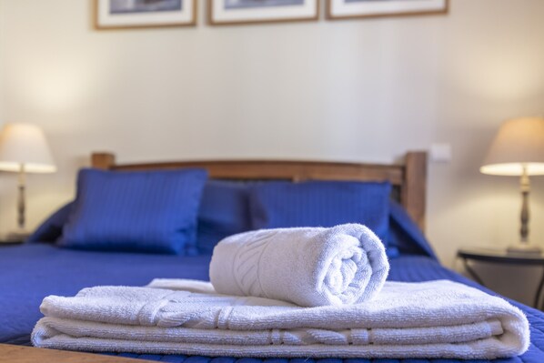 A neatly made bed with a folded white towel on top, a blue bedspread, and matching blue pillows.
