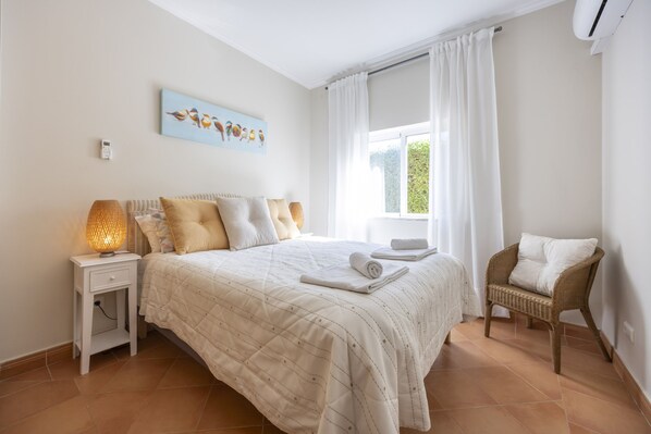 A bedroom with a bed, a nightstand, a lamp, a chair, and a window with curtains.