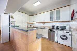 A modern kitchen with white cabinets, a granite countertop, a built-in oven, a microwave, a dishwasher, and a washing machine.