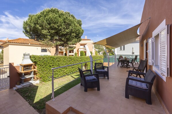 Une terrasse extérieure aménagée avec des meubles en osier, un barbecue et un grand arbre.