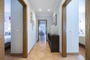 A hallway with wooden doors, a console table with a decorative vase, and a bed with a patterned bedspread in the background.
