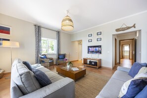 Un salon moderne comprenant un ensemble de canapés, une table basse, un téléviseur et un fauteuil en osier.
