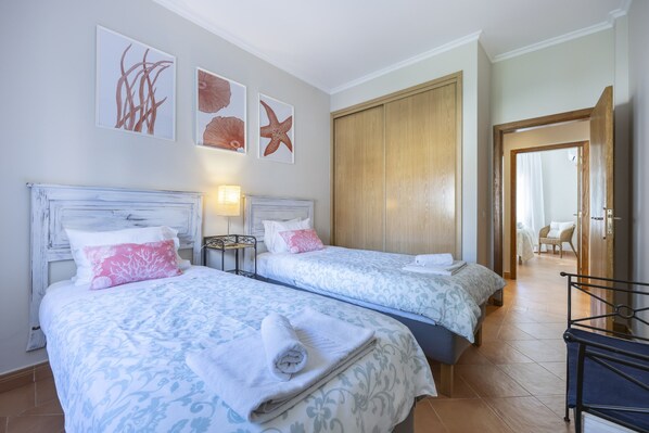 A hotel room with two beds, a wooden wardrobe, and a view of the hallway.