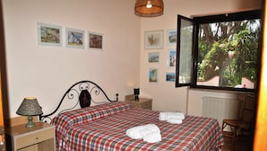 Une chambre avec deux lits, une table de chevet, une lampe, une chaise et une fenêtre donnant sur des arbres.