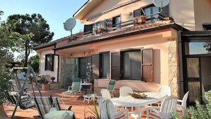 Une maison à deux étages dotée d’un patio aménagé avec des meubles d’extérieur, des antennes paraboliques et des plantes en pot.
