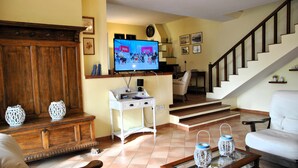Un salon avec un meuble en bois, un bureau blanc, une télévision et un escalier.