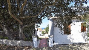 Un bâtiment blanc avec un chemin rouge menant à une porte, le tout entouré d’arbres.