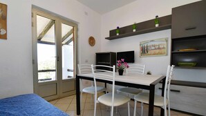Une pièce comprenant un lit, une table à manger avec des chaises, un téléviseur et des étagères avec des plantes.