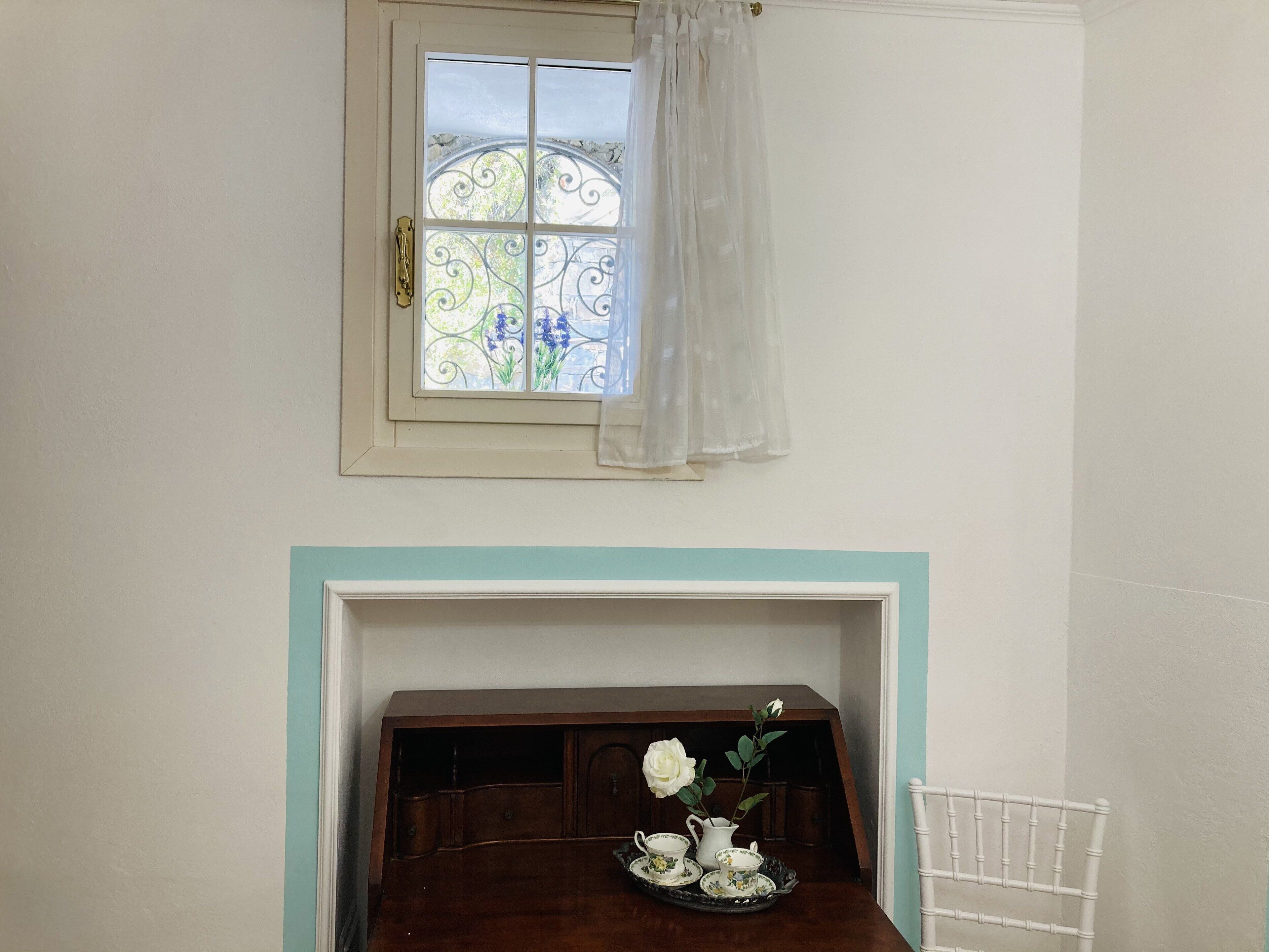 Una habitación con ventana, una mesa con juego de té y una silla blanca.