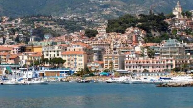 A coastal cityscape with a marina, buildings with varied architectural styles, and a backdrop of hills. - Sanremo: Apartment in Provencal villa with garden (Sanremo)