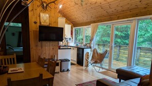 Ein Interieur einer Holzhütte mit Essbereich, Küche und einer großen Glasschiebetür, die auf eine Terrasse im Freien führt.