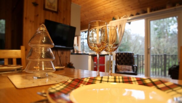 Ein Holzinterieur mit einem Esstisch, zwei Weingläsern und einem tellerförmigen Geschirr mit Karomuster.
