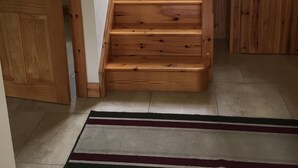 Una escalera de madera que lleva a un piso superior, una puerta a la izquierda y una ventana con vistas a árboles.