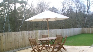 Un patio con mesa y sillas, cerca de madera y césped.