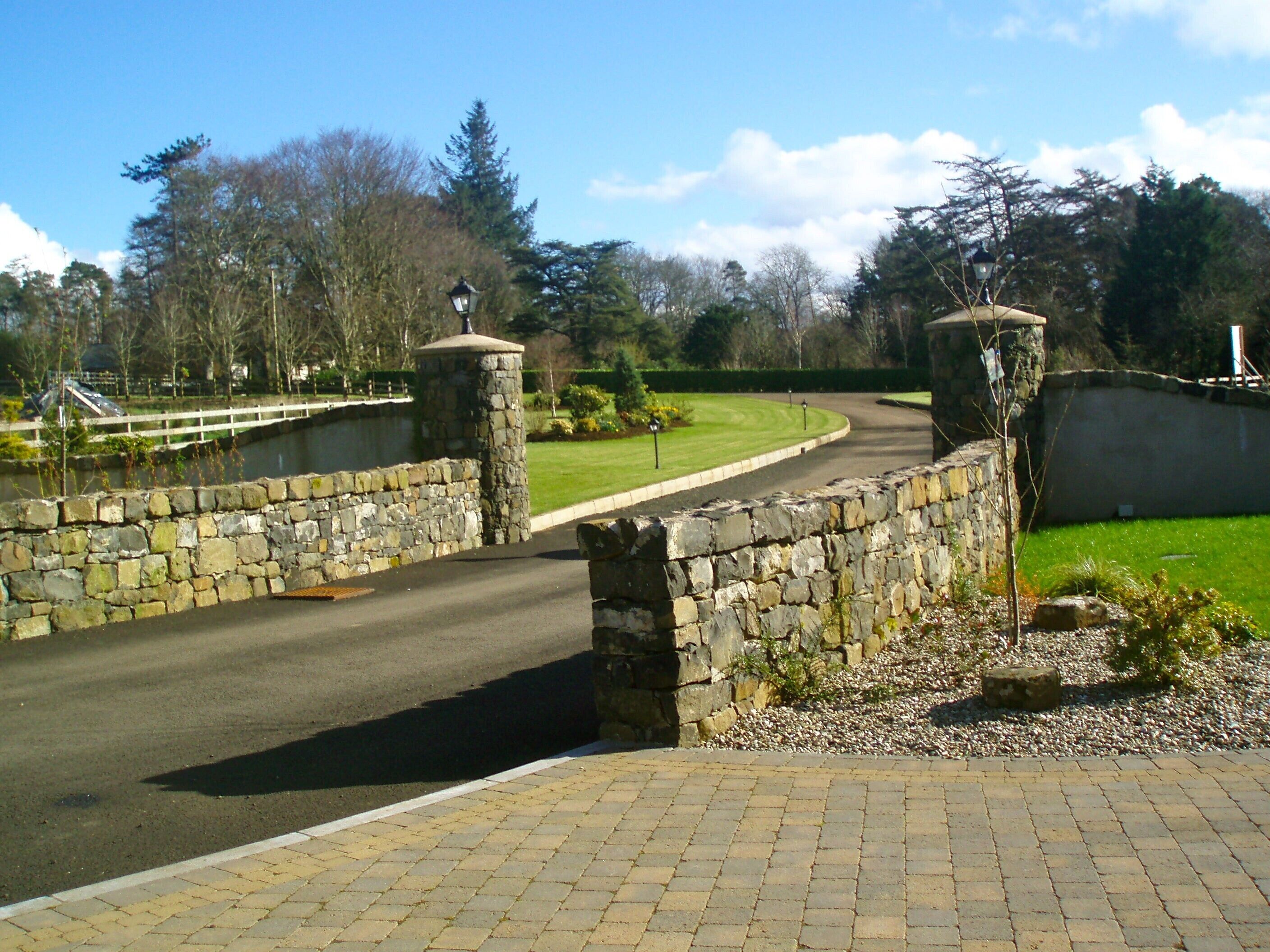 A stone bridge over a road with a stone wall on one side and a grassy area with trees on the other.