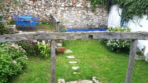A stone-walled garden with a wooden pergola, potted plants, and a blue table and chairs.