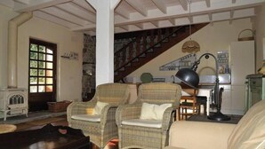 A cozy living room with wicker chairs, a sofa, a wooden table, and a staircase leading to an upper level.