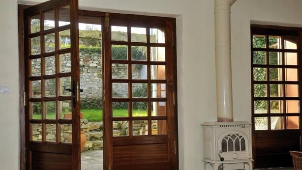 A room with a wooden door leading to a garden, a white stove, and a stone wall.