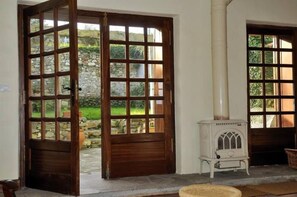 Una habitación con una puerta de madera que da a un jardín, una estufa blanca y un muro de piedra.