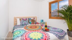 Een slaapkamer met een bed, kleurrijk beddengoed, een fles champagne en een kamerplant.