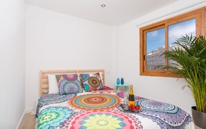A bedroom with a bed, colorful bedding, a bottle of champagne, and a potted plant.