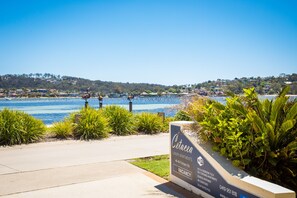 A sign for luxury apartments with a view of a body of water and hills in the background. - Cetacea Luxury Apartments (Merimbula)