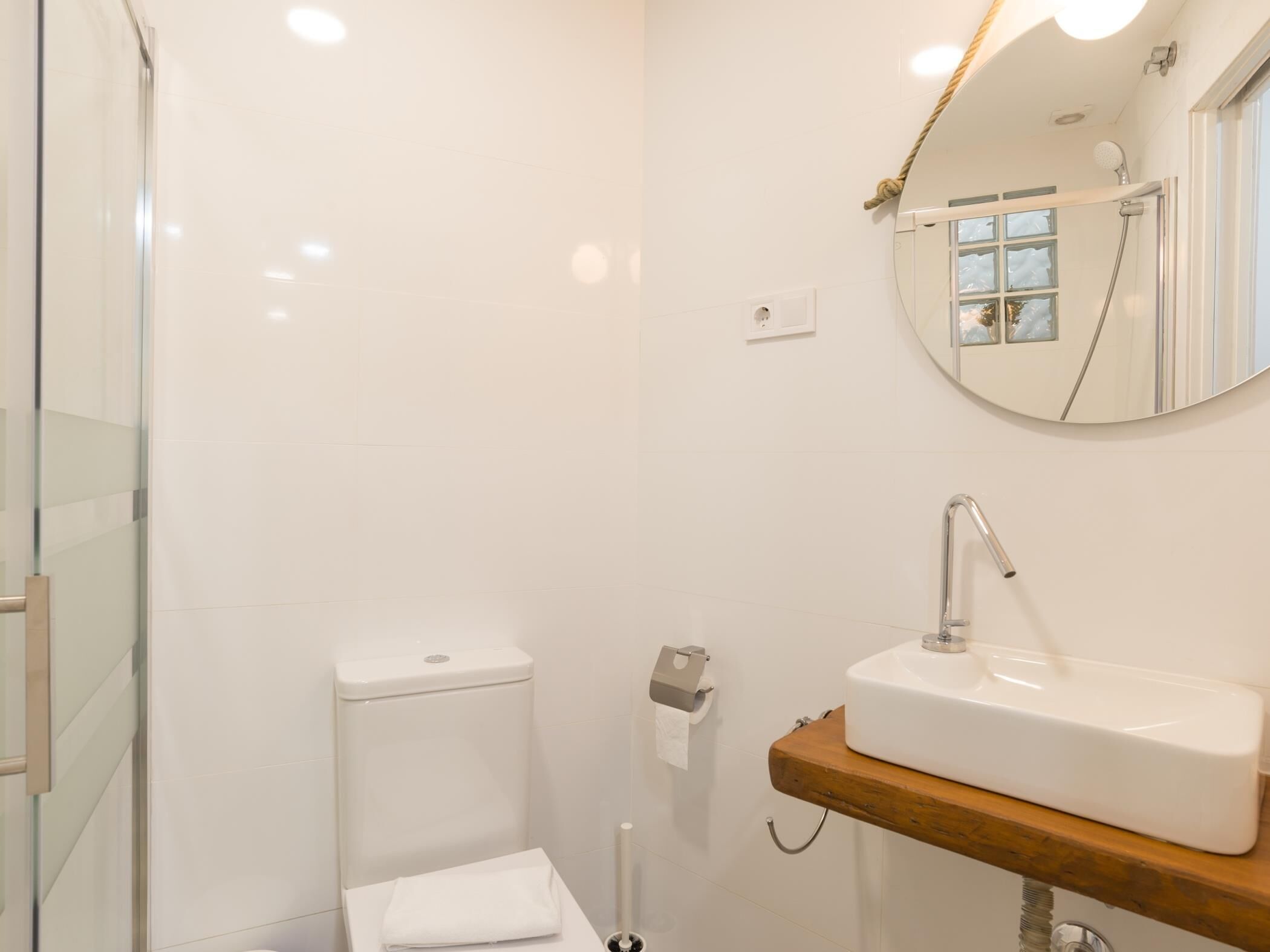 Un bany modern amb una cabina de dutxa de vidre, un vàter blanc i un lavabo de fusta amb un rentapeus.