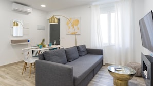 Ein modernes Wohnzimmer mit einem grauen Sofa, einem Esstisch mit Stühlen, einem Fernseher und einem Couchtisch.