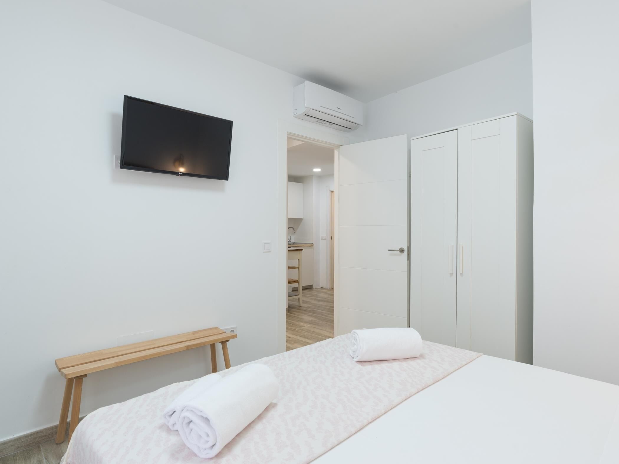 Ein Hotelzimmer mit Bett, Wandfernseher, Kleiderschrank und einer kleinen Holzbank.