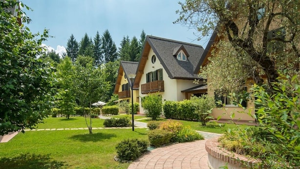 Een tweelaags huis met een gebogen oprit, omringd door keurig onderhouden gazons en bomen.