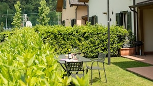 Een woongebouw met een schuin dak, een terras met een tafel en stoelen, en uitzicht op een heuvel met andere gebouwen.
