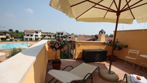 A rooftop terrace with a pool, lounge chairs, a table, and an umbrella.