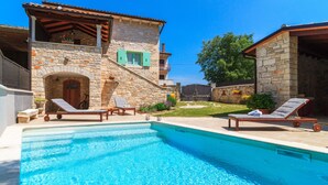 Un edificio de piedra con piscina, dos sillones de descanso y un pequeño jardín.