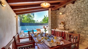Una mesa de madera con desayunos, una pared de piedra y vista a una piscina.