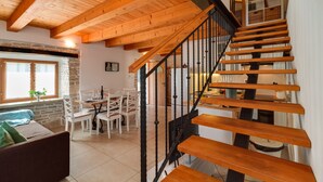 Una escalera de madera con barandales negros que conduce a un segundo piso. Abajo se puede ver un comedor con sillas blancas y una mesa.